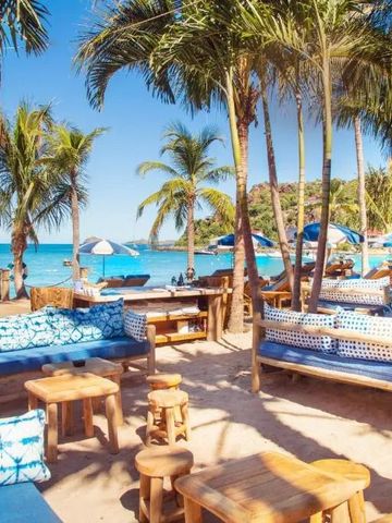 Strandabschnitt mit Palmen und gemütlichen Sitzbereichen unter blauem Himmel