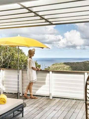 Frau blickt von Terrasse mit Sonnenschirm auf bewaldete Landschaft und Meer