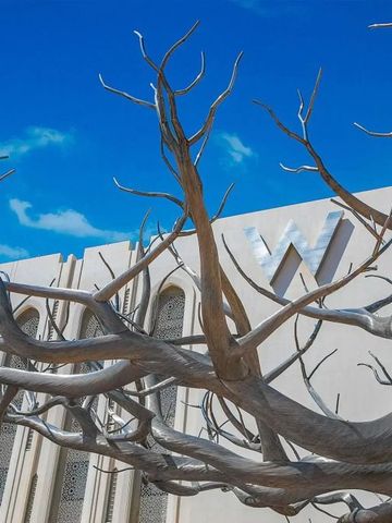 Fassade des Hotels mit skulpturalen Bäumen vor blauem Himmel