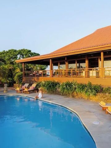 Pool mit Sonnenliegen und tropischer Vegetation neben einer Holzvilla