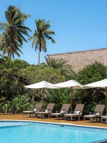 Pool mit Palmen und Strohdachgebäude im Hintergrund