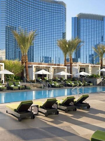 Poolbereich mit Liegen und Palmen vor modernen Gebäuden