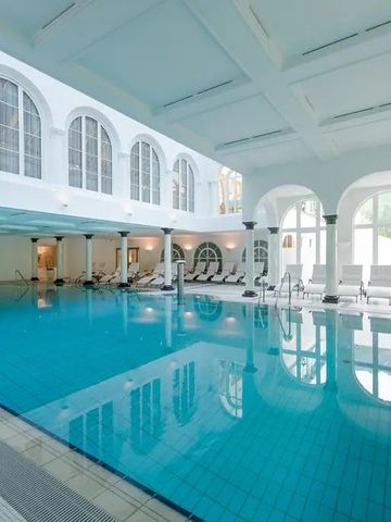 Innenansicht eines luxuriösen Hotelpools mit Liegestühlen und hohen Fenstern
