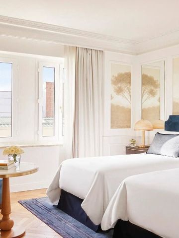 Elegantes Hotelzimmer mit zwei Einzelbetten und großen Fenstern mit Vorhängen.