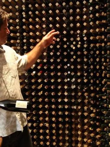 Weinkeller mit diversen Flaschen in Regalen und einer Person, die eine Flasche auswählt.