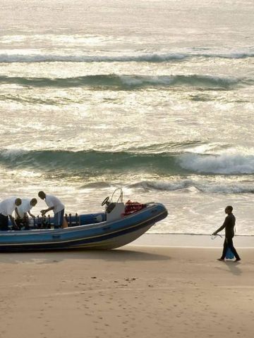 Boot am Strand bei Sonnenuntergang mit Besatzung in weißer Kleidung