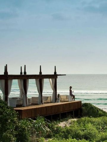 Holzterrasse mit Sitzgelegenheiten und Vorhängen direkt am Meer