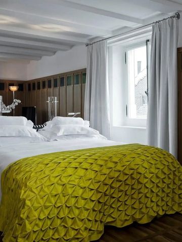 Helles Zimmer mit gelbem Überwurf, großzügigem Fenster und eleganten Vorhängen im Widder Hotel