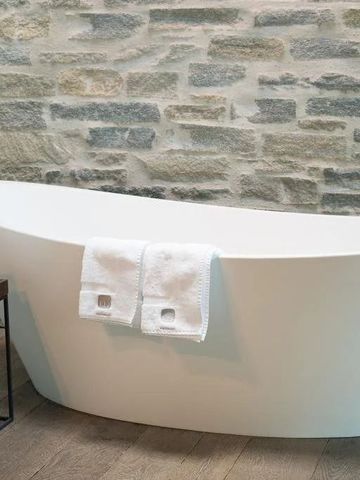 Moderne freistehende Badewanne vor Natursteinwand im Hotel Wiesergut