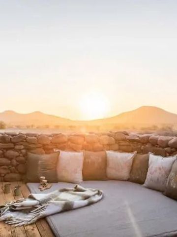 Gemütliche Terrasse mit Kissen und Blick auf die Wüstenlandschaft bei Sonnenuntergang