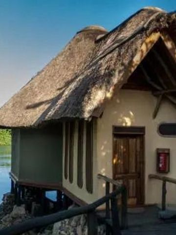 Hütte mit Strohdach am Wasser vor üppigem Grün