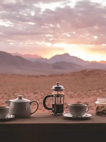 Idyllischer Teetisch mit Gebäck vor einer beeindruckenden Wüstenlandschaft im Sonnenuntergang.
