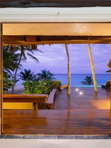 Holzterrasse mit Blick auf Strand und Meer, umgeben von Palmen bei Sonnenuntergang.