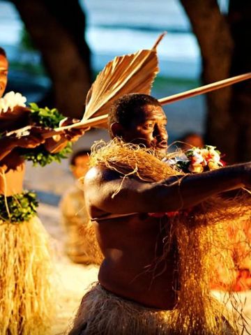 Traditionelle fidschianische Tänzer in Bastkleidung bei Sonnenuntergang.
