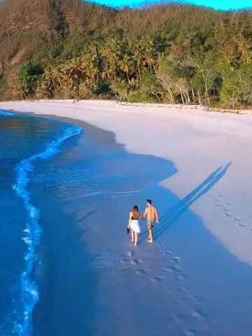 Paar spaziert Hand in Hand auf weißem Sandstrand bei Yasawa Island Resort.