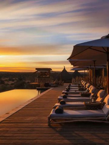 Infinity Pool und Liegen auf einer Holzterrasse bei Sonnenuntergang.