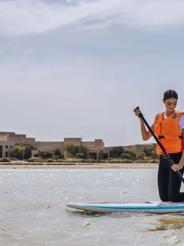 Person paddelt auf einem Board auf dem Meer mit Gebäude im Hintergrund.