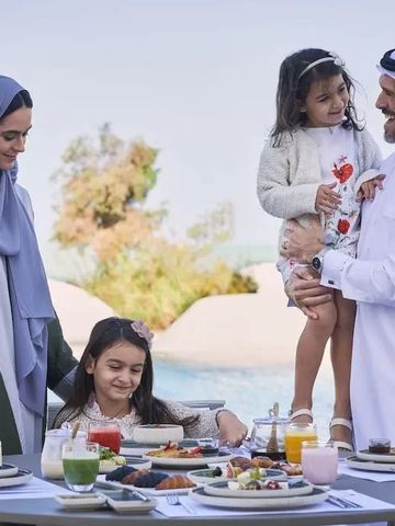 Familie isst an einem Tisch im Freien mit Pool im Hintergrund.