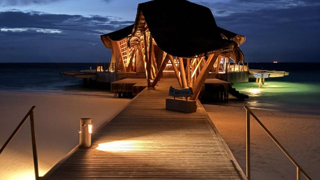 Beleuchteter Holzsteg zum Restaurant Madi Hiyaa mit Bambusdach zur blauen Stunde