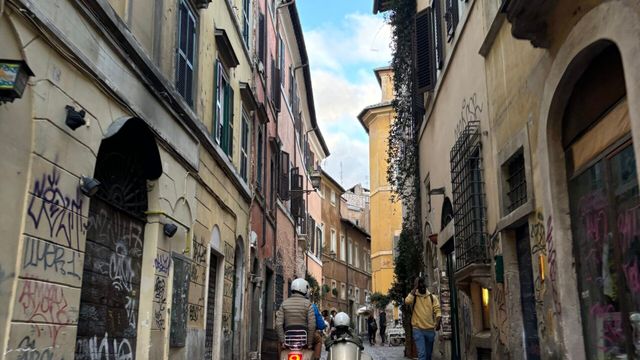 Malerische Stadtstraße mit historischen Gebäuden und Vespa-Fahrern