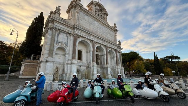 Gruppe von Leuten auf farbigen Vespas vor historischem Brunnen