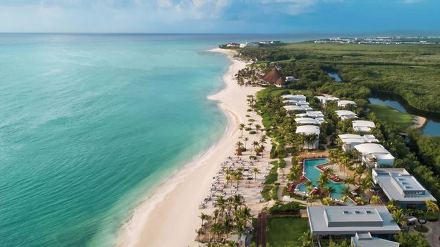 Luftaufnahme eines weißen Sandstrandes am türkisfarbenen Meer und der Anlage.