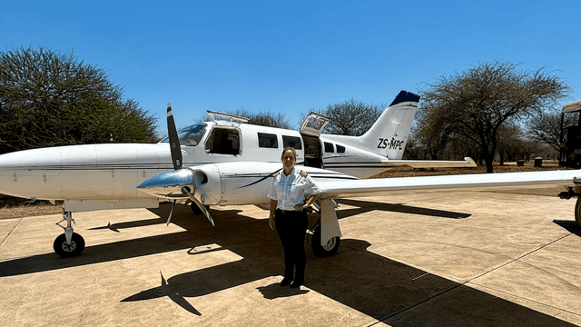 Pilotin steht stolz vor einem weißen Kleinflugzeug auf einem Flugfeld
