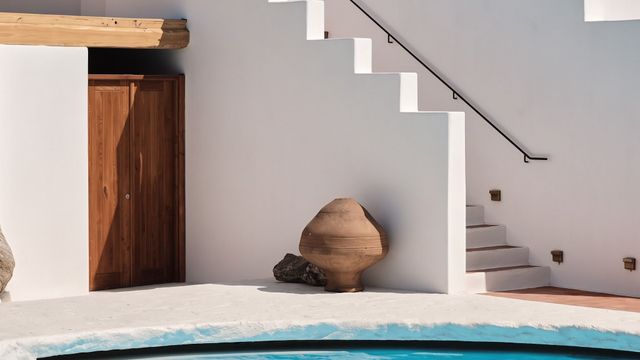 Weiß gekalktes Gebäude mit Außentreppe, Holztür und Pool im Vordergrund.