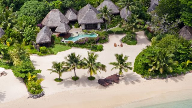 Luftaufnahme einer Villa mit Reetdach am Sandstrand mit Pool und Palmen.