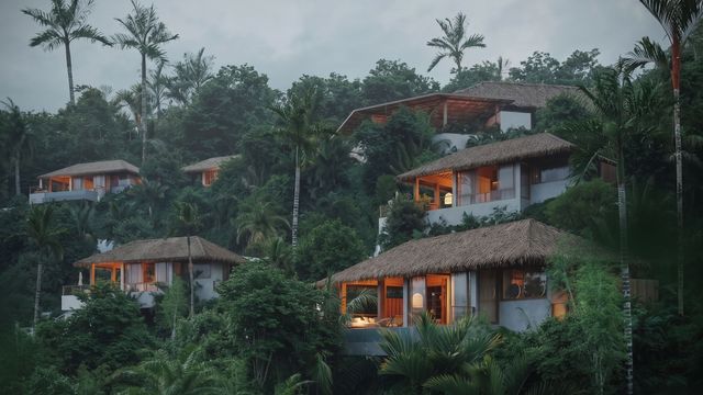 Bungalows mit Strohdächern an einem dichten bewaldeten Hang in der Dämmerung.