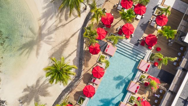 Luftaufnahme eines luxuriösen Pools mit roten Sonnenschirmen und Palmen