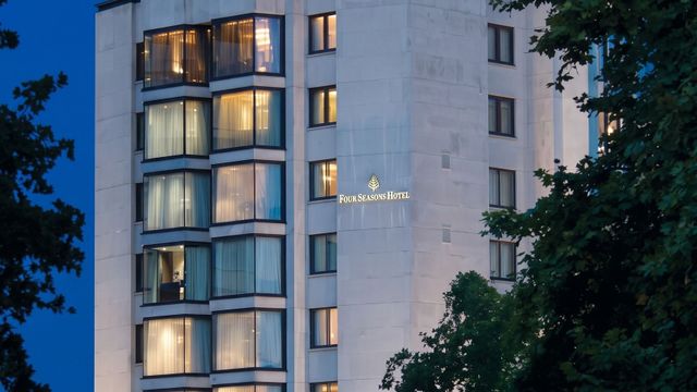 Beleuchtete Fassade des mehrstöckigen Hotelgebäudes bei Dämmerung mit Bäumen im Vordergrund.