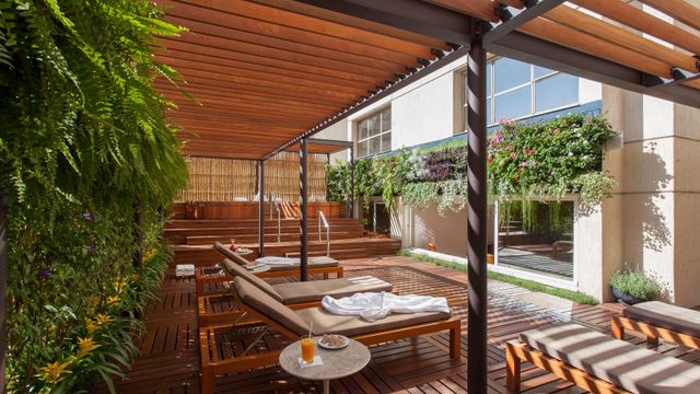 Holzterrasse mit Sonnenliegen unter einer Holzpergola und begrünter Wand.