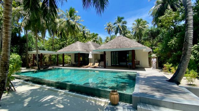 Luxuriöse Villa mit privatem Pool, umgeben von Palmen und tropischer Natur auf den Malediven, bei strahlend blauem Himmel.