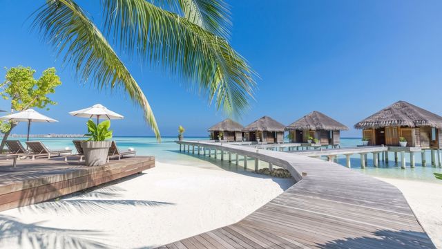 Ein Holzsteg führt zu traditionellen Wasserbungalows im türkisfarbenen Meer.