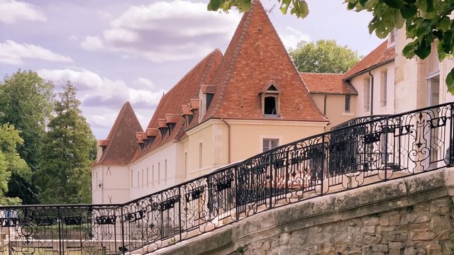 Historisches Gebäude mit roten Ziegeldächern hinter einer Steinmauer mit Geländer.