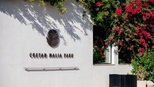 Weiße Außenwand des Gebäudes mit dem Namenszug des Hotels und blühenden Bougainvillea-Pflanzen.