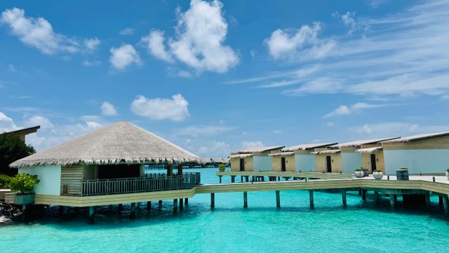 Überwasservillen vor kristallklarem türkisfarbenem Wasser unter blauem Himmel