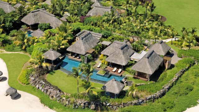 Luftaufnahme von Reetdach-Villas mit privaten Pools inmitten tropischer Bepflanzung am Meer.