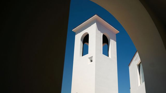 Weißer Turm der Hotelanlage unter blauem Himmel, eingerahmt von einem Rundbogen.