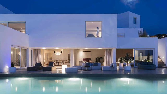 Moderne Villa bei Nacht mit beleuchtetem Pool und elegantem Innenraum