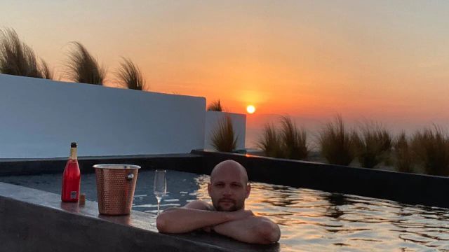 Mann im Pool mit Champagnerflasche bei Sonnenuntergangslandschaft