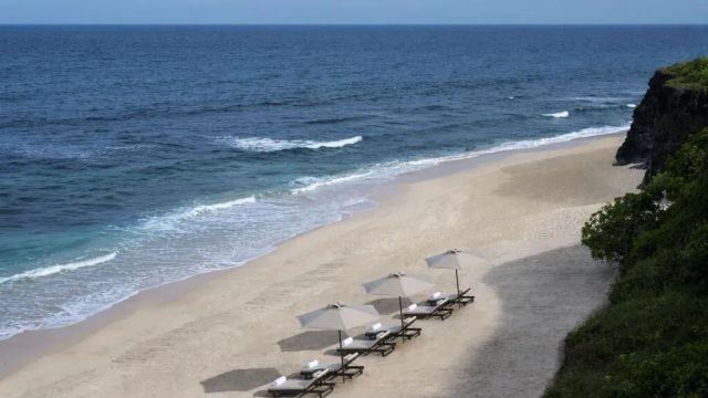 Einsamer Sandstrand mit vier Liegen und Sonnenschirmen am Meer.