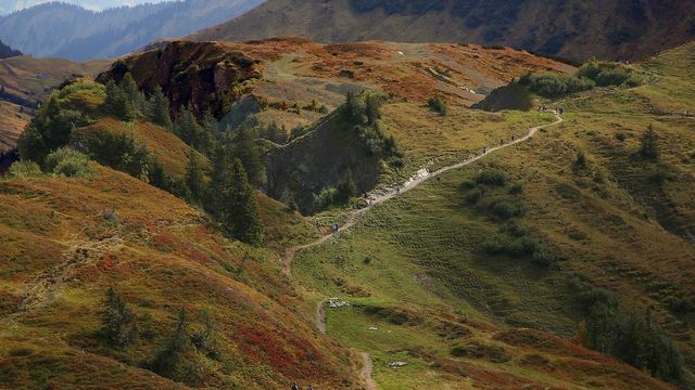 Gewundener Wanderweg durch grüne und rötliche Hügellandschaft.