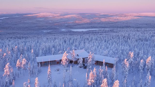 Luftbild der Octola Lodge zwischen verschneiten Bäumen, dahinter Fjells im rosa Winterlicht