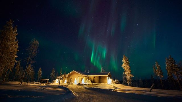 Grüne Nordlichter über der beleuchteten Lodge von Octola II in einer verschneiten Winternacht