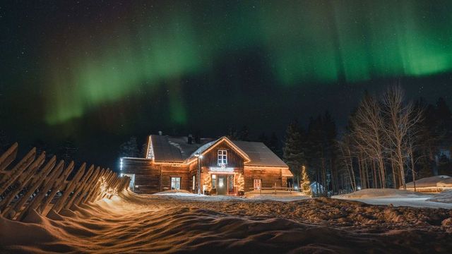 Historisches Holzhaus von Reindeer Manor mit beleuchtetem Eingang unter grünen Nordlichtern bei Nacht