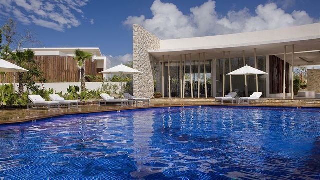 Modernes, luxuriös eingerichtetes Resortzimmer im Rosewood Mayakoba mit großen Panoramafenstern, gemütlicher Sitzecke, stilvollen Holzböden und Ausblick auf tropische Gartenlandschaft.