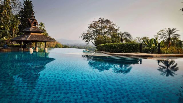 Infinity-Pool des Anantara Golden Triangle Elephant Camp & Resort mit traditionellem Pavillon und Blick auf üppige tropische Landschaft und ferne Hügel.