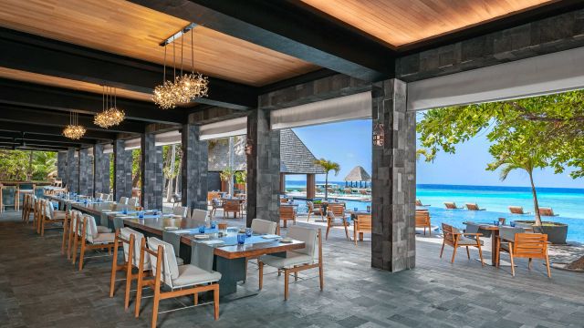 Restaurant Manzaru im Anantara Kihavah Maldives Villas mit offenem Design, stilvollen Sitzplätzen und Blick auf Pool, Palmen und das türkisblaue Meer.